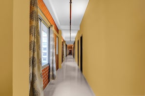 A corridor with a tiled floor, a window with a curtain, and a brick wall. - Townhouse Oak Siliguri (Siliguri)