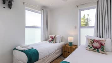 Une chambre d’hôtel avec deux lits, un ventilateur de plafond, une table de chevet avec une lampe et des fenêtres avec des rideaux.