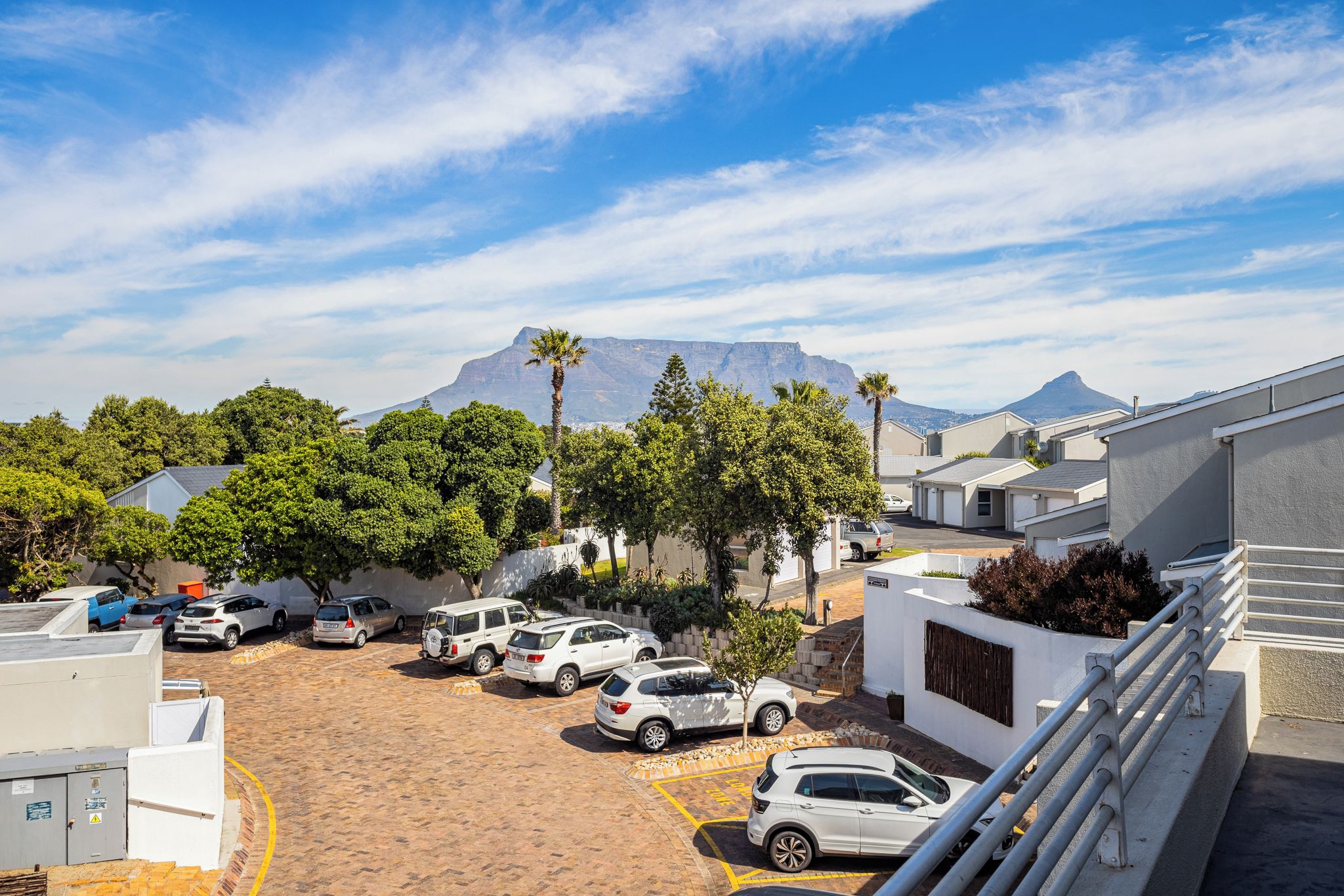 A parking area with several cars, a mountain in the background, and a building with a white facade.