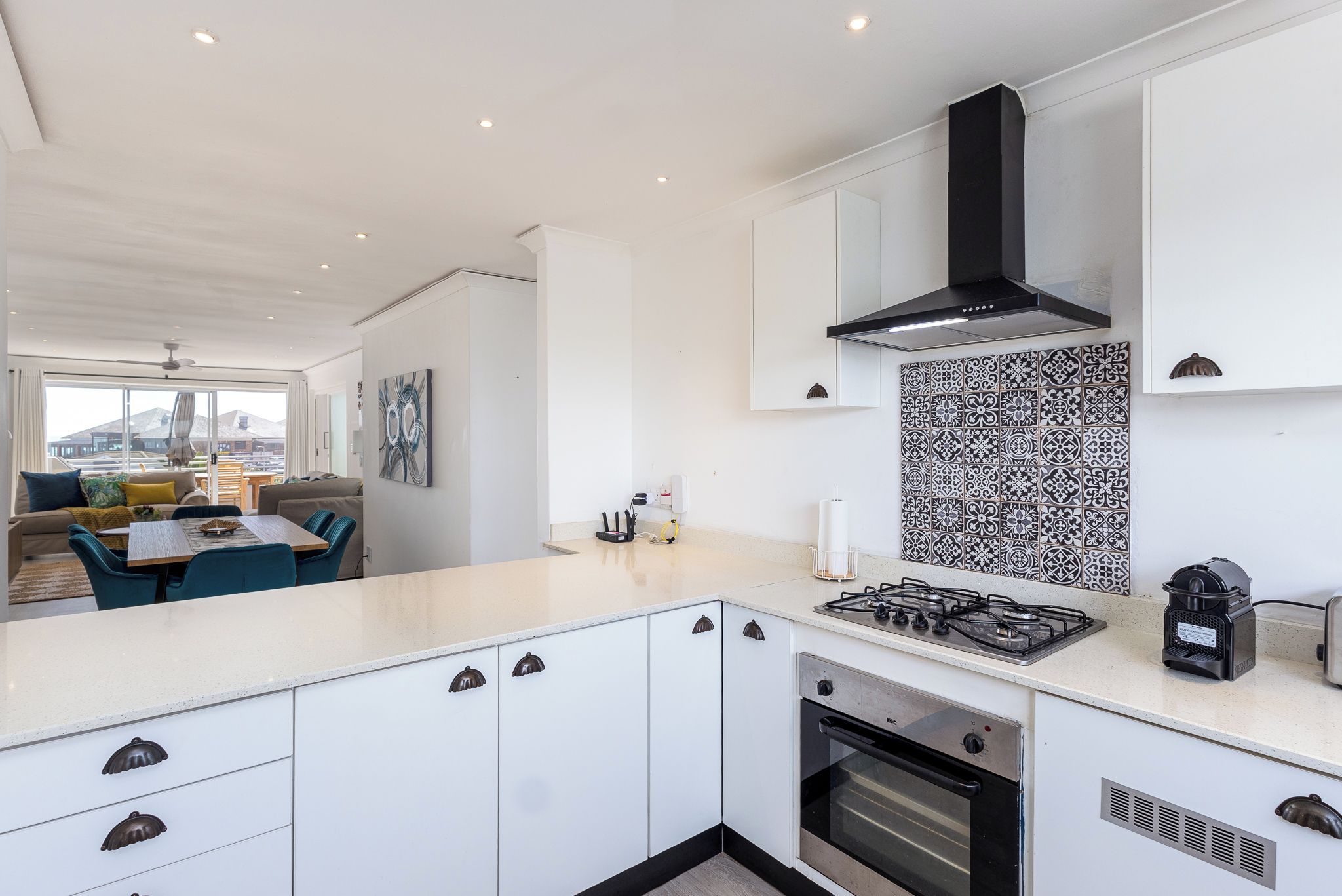 Une cuisine moderne avec des meubles blancs, une hotte noire et un pare-feu décoré.