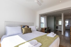 A modern bedroom with a large bed, a desk, and a bathroom visible through an open doorway. - Beachfront 2br, Sea Views and Sunsets (Cape Town)