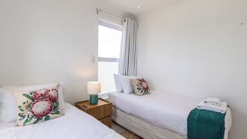 Une chambre d’hôtel avec deux lits, une table de chevet avec une lampe et une fenêtre avec des rideaux.