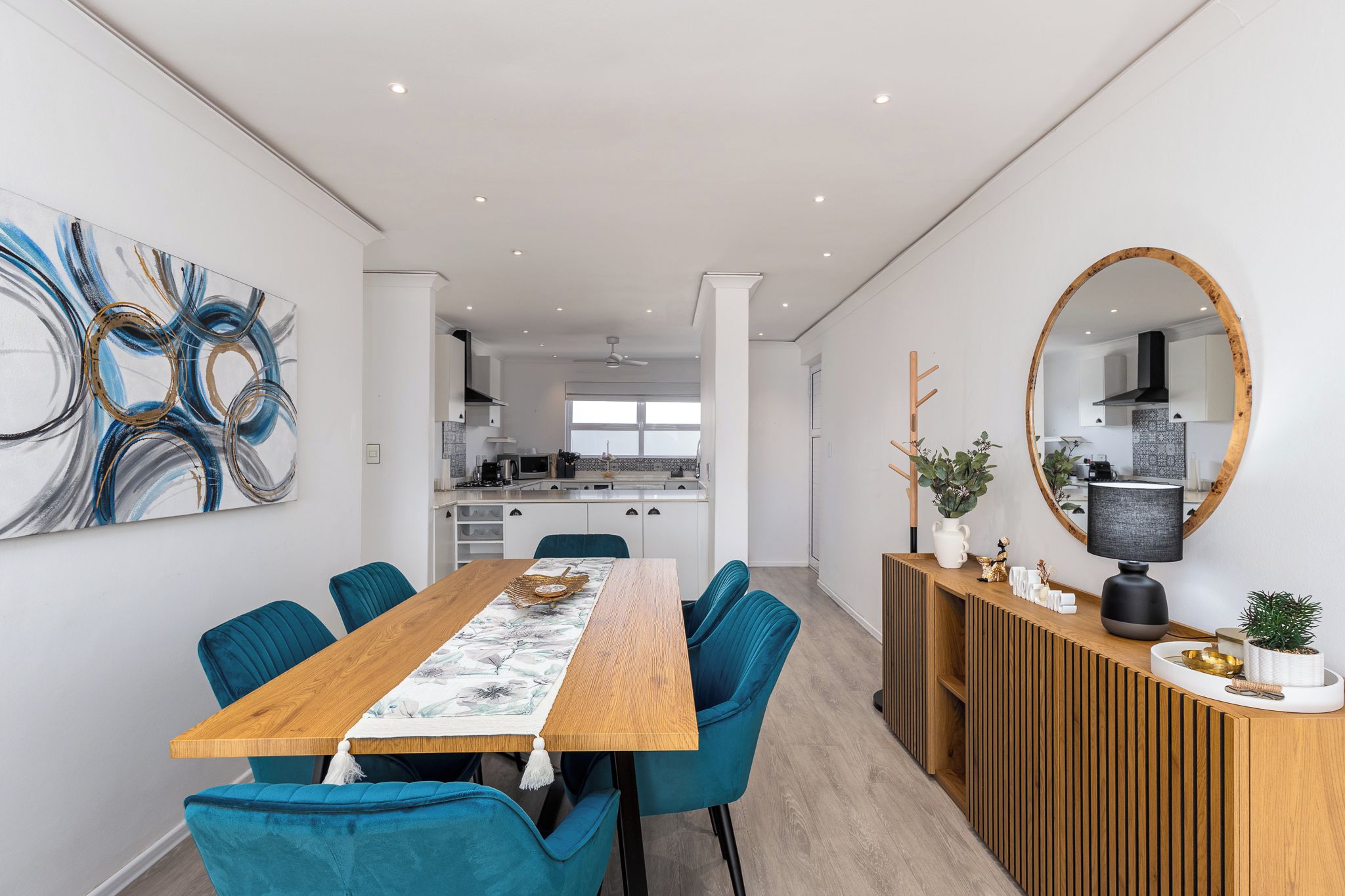 A modern dining area with a wooden table, teal chairs, and a decorative table runner.