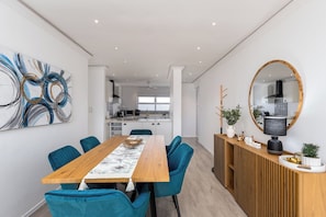 A modern dining area with a wooden table, teal chairs, and a decorative table runner. - Beachfront 2br, Sea Views and Sunsets (Cape Town)