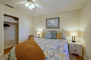 Ein Schlafzimmer mit einem Bett, Nachttischlampen, einem Deckenventilator, einem gerahmten Bild an der Wand und einem Kleiderschrank mit Kleidung.