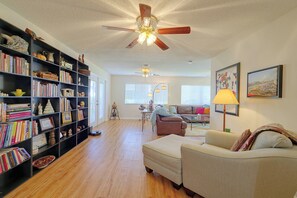 Ein geräumiges Wohnzimmer mit Bücherregal, Deckenventilator, einer Couch und einem Gemälde an der Wand.