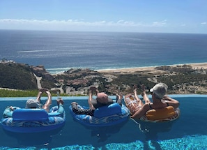 Drei Personen schwimmen in einem Pool mit Blick auf den Ozean und den Strand.