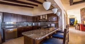 A modern kitchen with granite countertops, dark wooden cabinets, and a central island with bar stools. - PBMC · Pueblo Bonito Montecristo Owners Estate 3BR3B (Cabo San Lucas)