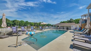 Ein Swimmingpool mit Liegestühlen und Sonnenschirmen, umgeben von einem Zaun und Bäumen.