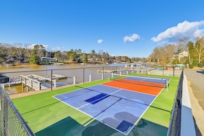 An outdoor tennis court with a view of a lake and buildings in the background.