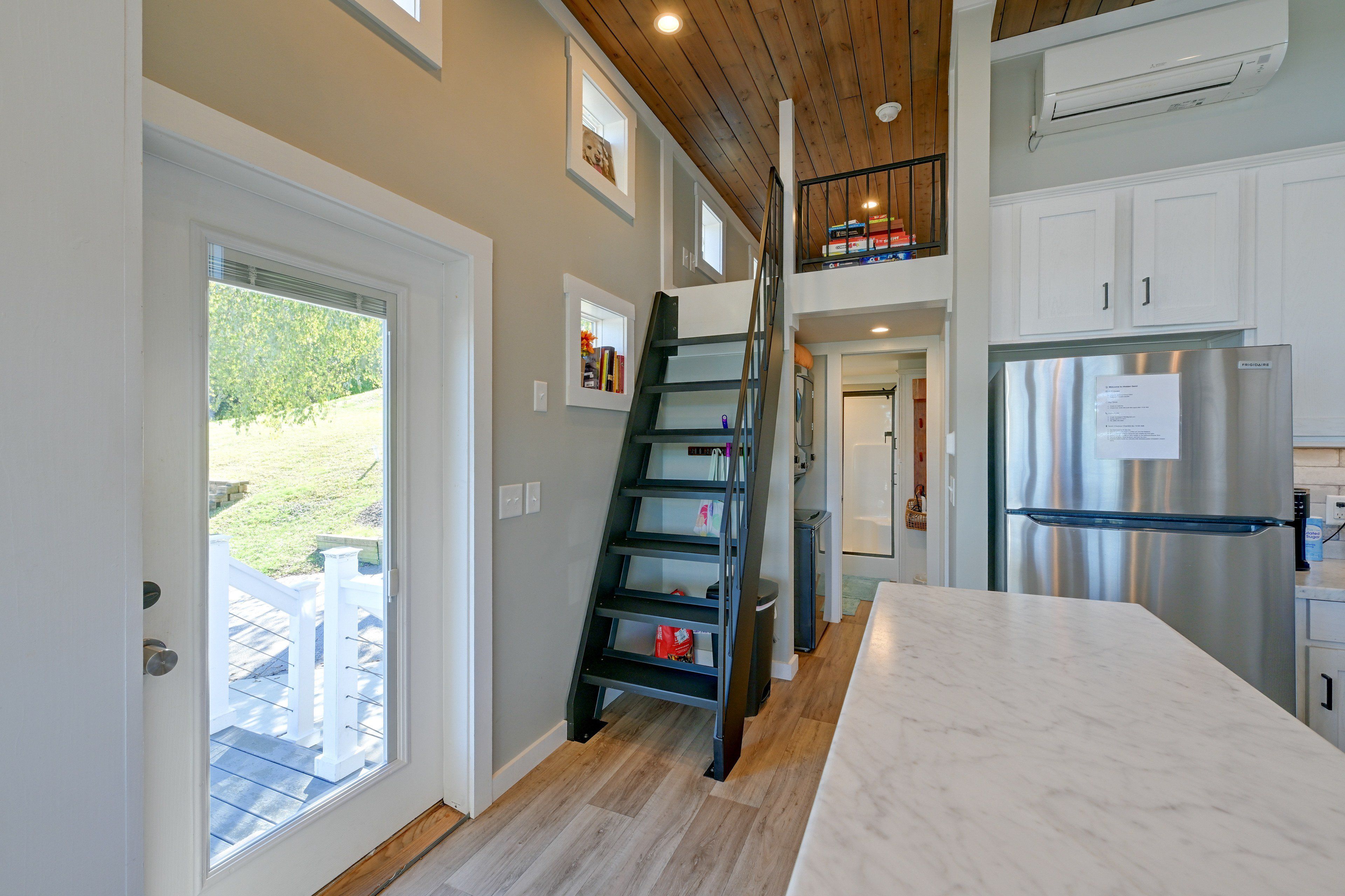 A modern kitchen with a stainless steel refrigerator, a wooden staircase, and a view of the outdoors.