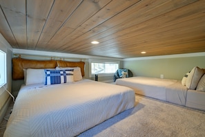 A bedroom with two beds, a wooden ceiling, and a window.