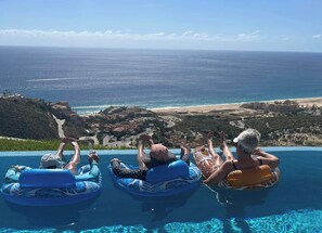 Drei Personen schwimmen in einem Pool mit Blick auf den Ozean und den Strand.
