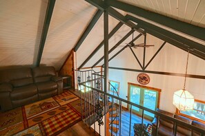 A loft-style room with a high ceiling, exposed beams, a leather sofa, a patterned rug, and a staircase leading to an upper level. - Hocking Hills Area Retreat: Relax & Explore! (Rockbridge)