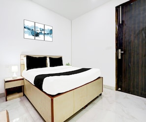 A bedroom with a bed, bedside table, lamp, and a wall-mounted artwork. - Classic Maharaja Grand (New Delhi)