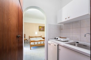A compact kitchen with a sink, stove, and a bed visible through an archway. - Archontiko Studios (Zakynthos)