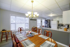 Un coin repas avec une table et des chaises en bois, un lustre et une cuisine en arrière-plan.