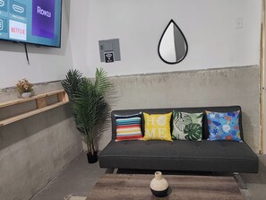 En moderne stue med en grå sofa, et fladskærms-TV, et Wi-Fi symbol, et dekorativt spejl og en lille potteplante.