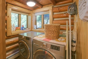 A laundry area with two front-loading washing machines, a drying rack, and a window with a view of trees. - Waterfront Lake Charlevoix Cabin 8 Mi to Boyne Mtn (Boyne City)