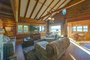 Ein Holzblockhaus-Interieur mit Kamin, Fernseher, Essbereich und Blick ins Freie.