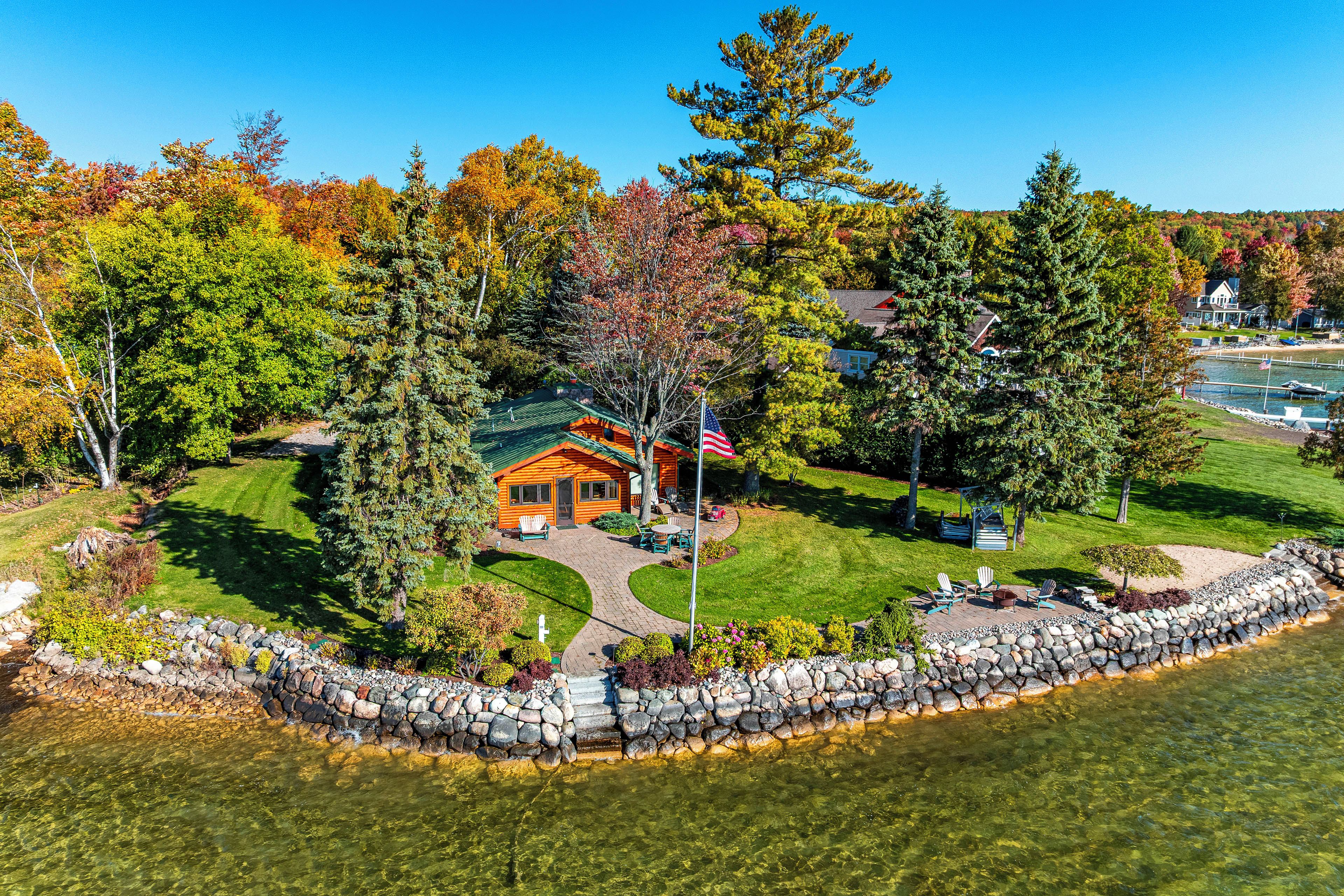A lodge with a stone dock, a flagpole, and a clear view of the surrounding autumn foliage.
