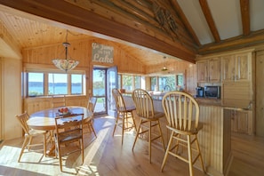 A wooden cabin interior with a dining area, kitchen, and large windows overlooking a lake. - Waterfront Lake Charlevoix Cabin 8 Mi to Boyne Mtn (Boyne City)