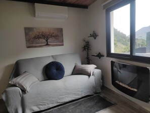 A living room with a sofa, a fireplace, a painting, and a window with a view. - Little Hideaway - São Vicente (Madeira)