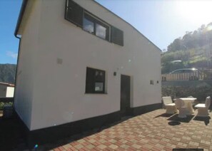 A two-story building with a flat roof, a small door, and a window. There are outdoor chairs and a table on a paved area. - Little Hideaway - São Vicente (Madeira)