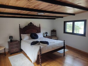 A bedroom with a wooden bed, two bedside tables, a nightstand, a window with a view, and a wooden ceiling. - Little Hideaway - São Vicente (Madeira)
