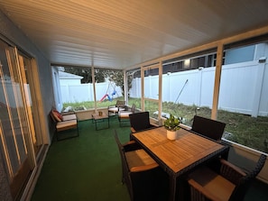 Eine überdachte Terrasse mit Tisch und Stühlen, einem kleinen Blumentopf und einer Schaukel im Hintergrund.