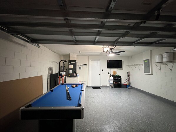 A pool table in a room with a ceiling fan, a mounted TV, and a water heater on the wall.