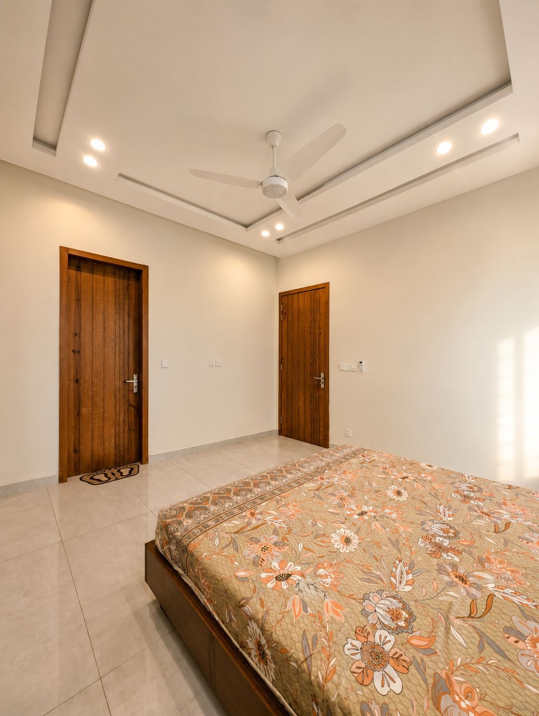 Une chambre à coucher comprenant un lit, deux portes, un ventilateur de plafond, un éclairage encastré et un tapis à motifs.