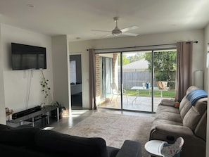 A living room with a flat-screen TV, a sofa, a coffee table, and a sliding glass door leading to a patio. - Spacious 3-Bedroom House Rental in Waterford, Australia (Waterford)