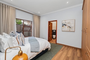 A bedroom with a bed, curtains, a window, a door, a painting, and a wardrobe. - Luxurious 4-Bedroom Villa with Private Pool in Hartbeespoort (Hartbeespoort)