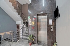 A hotel lobby with a staircase, an elevator, and a potted plant. - Signature Hotel Noida-62 (Noida)