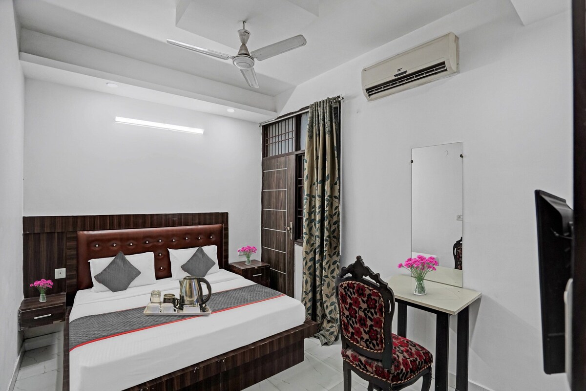 A hotel room with a bed, bedside table, chair, desk, mirror, and ceiling fan.