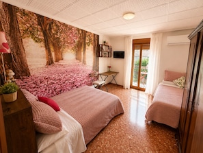A bedroom with a bed, a desk, a chair, a TV, and a balcony.