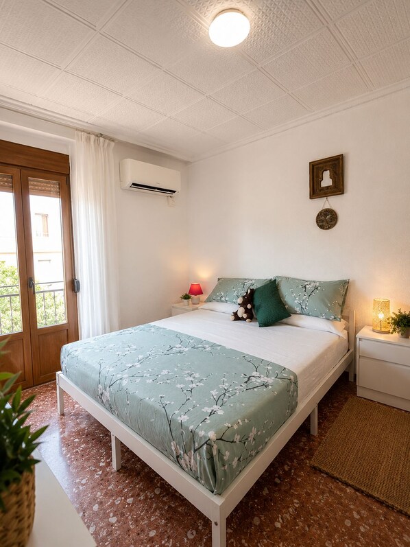 A bedroom with a bed, bedside lamps, an air conditioning unit, and a window with curtains.