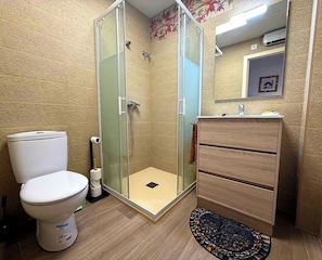 A bathroom with a toilet, a glass-enclosed shower, and a wooden vanity.