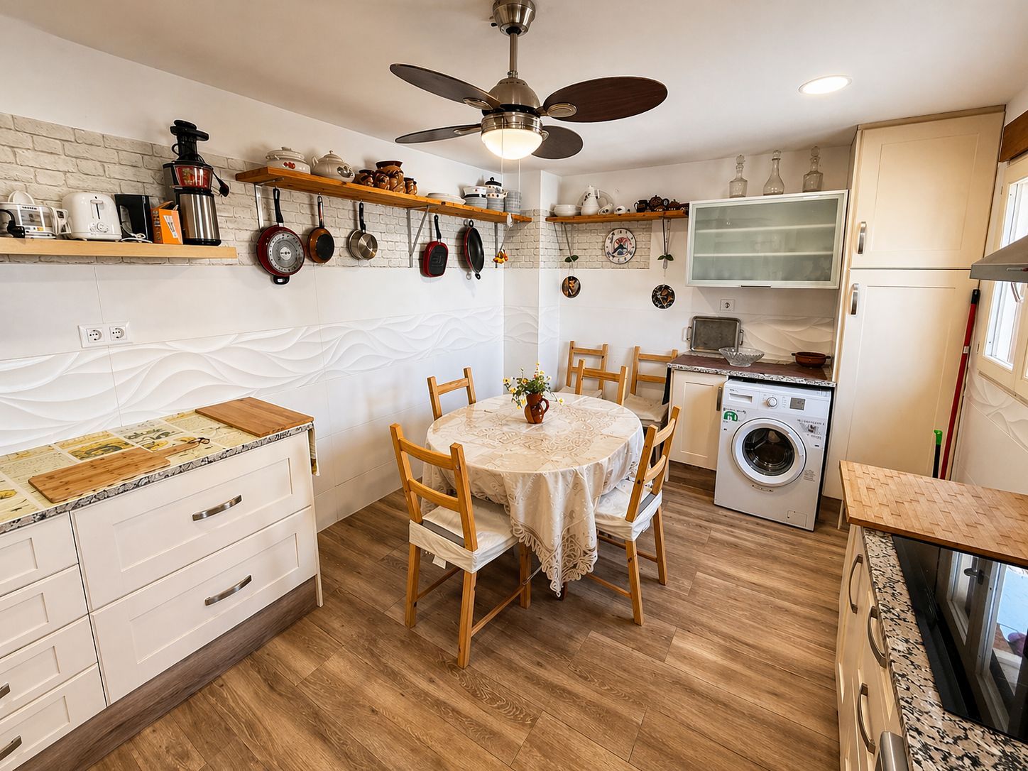 Una cucina compatta con un tavolo da pranzo, sedie di legno, una ventola a soffitto e una lavatrice.