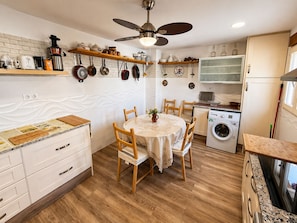 A compact kitchen with a dining table, wooden chairs, a ceiling fan, and a washing machine.
