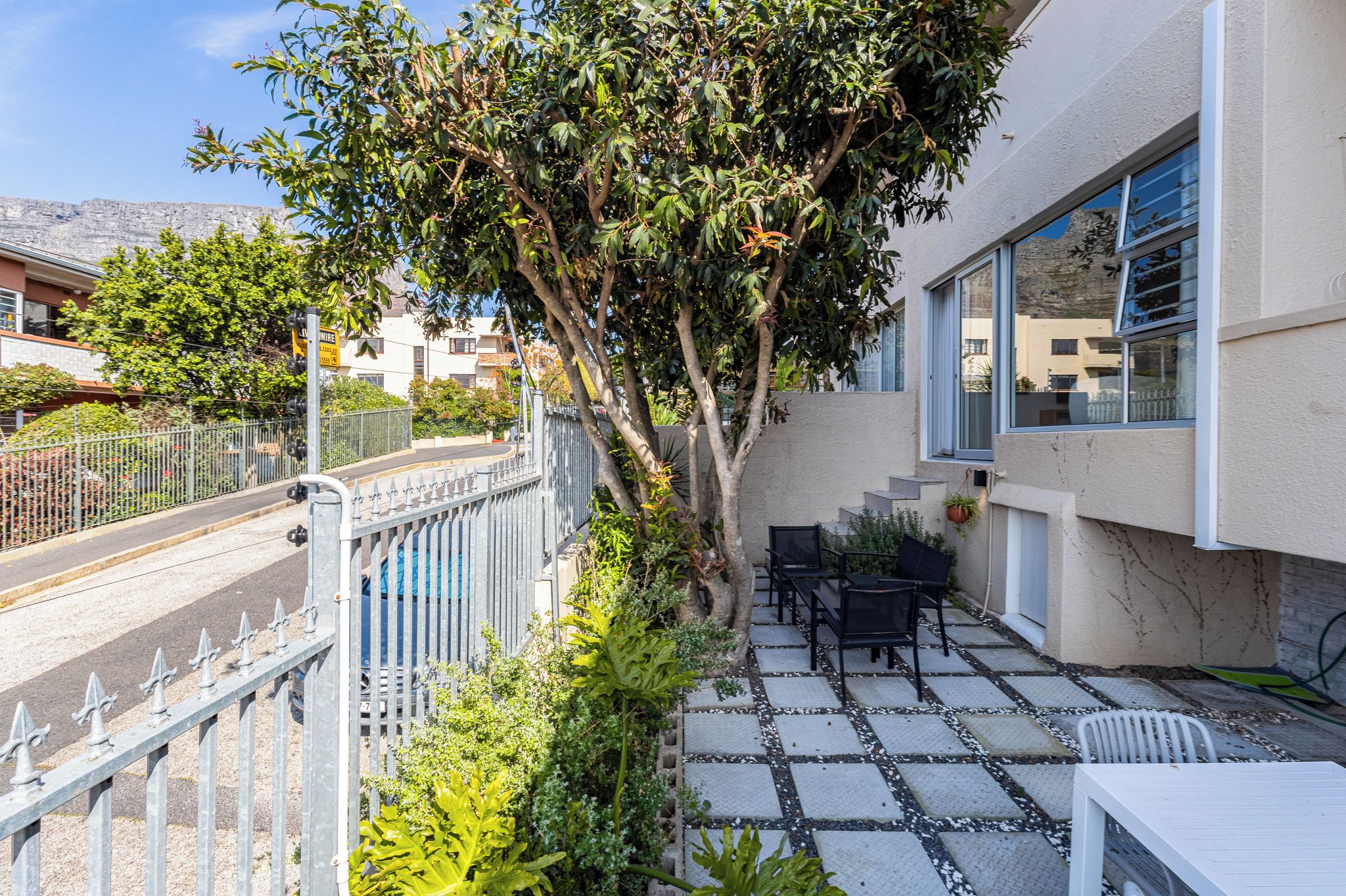 Zona residenziale con patio lastricato, mobili da esterno e un albero.