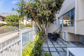 Zona residencial con un patio empedrado, mobiliario exterior y un árbol.