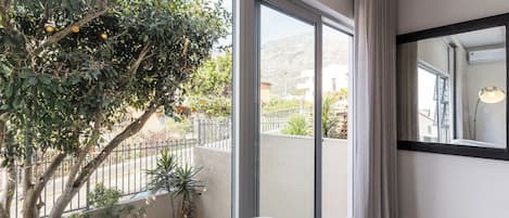A hotel room with a large sliding glass door leading to a balcony, a bed, a mirror, and a potted plant.