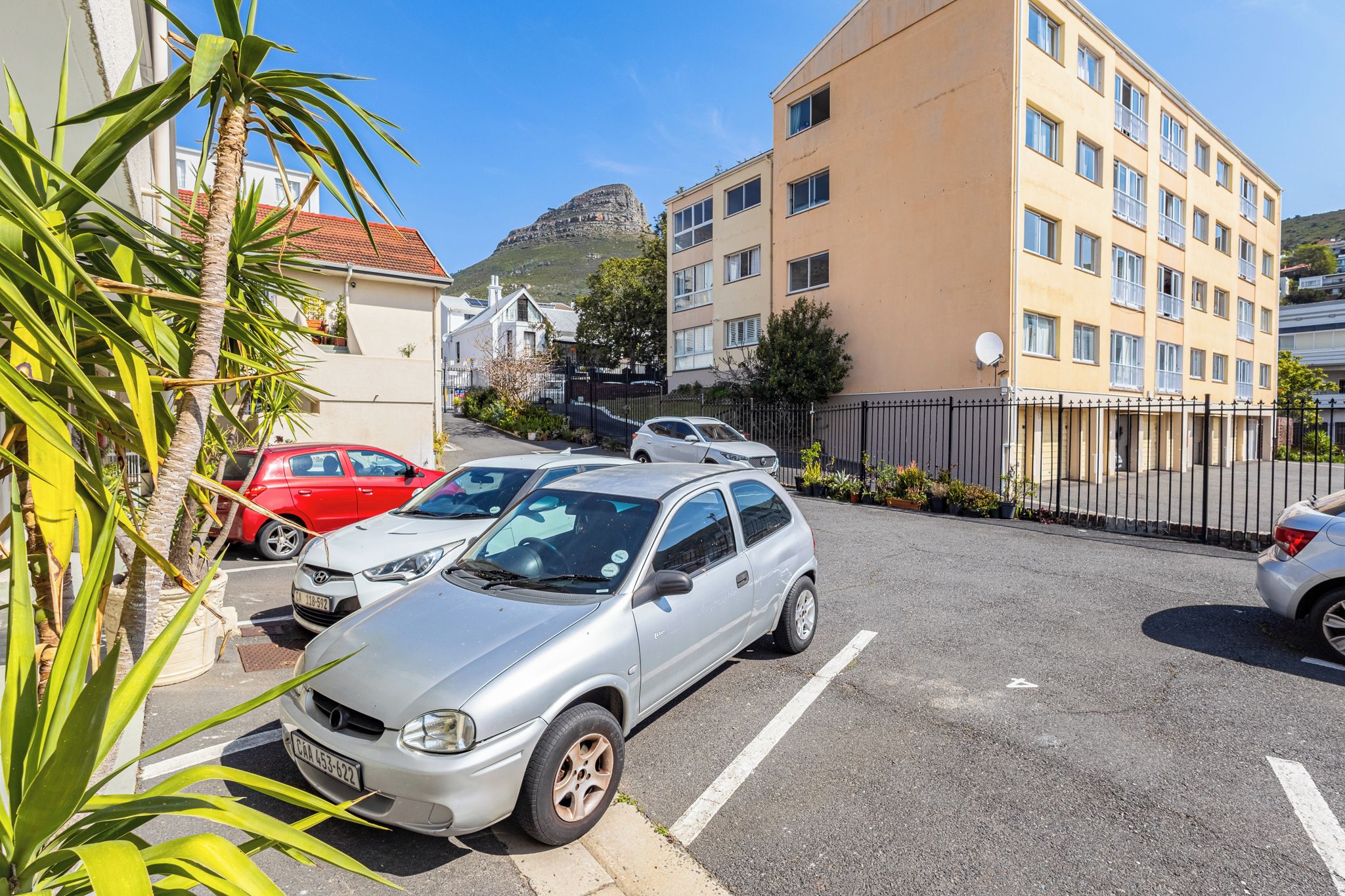 Ein Parkplatz mit mehreren Autos, ein Gebäude mit vielen Fenstern und eine Hügelkulisse im Hintergrund.