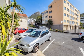 Un estacionamiento con varios autos, un edificio con muchas ventanas y una colina al fondo.