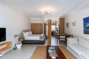Una sala de estar moderna con un sofá, una mesa de centro con revistas, un televisor y una zona de comedor con sillas y una mesa.