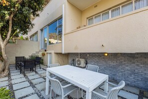 Un patio al aire libre con una mesa y sillas blancas, un muro de ladrillo y un árbol.