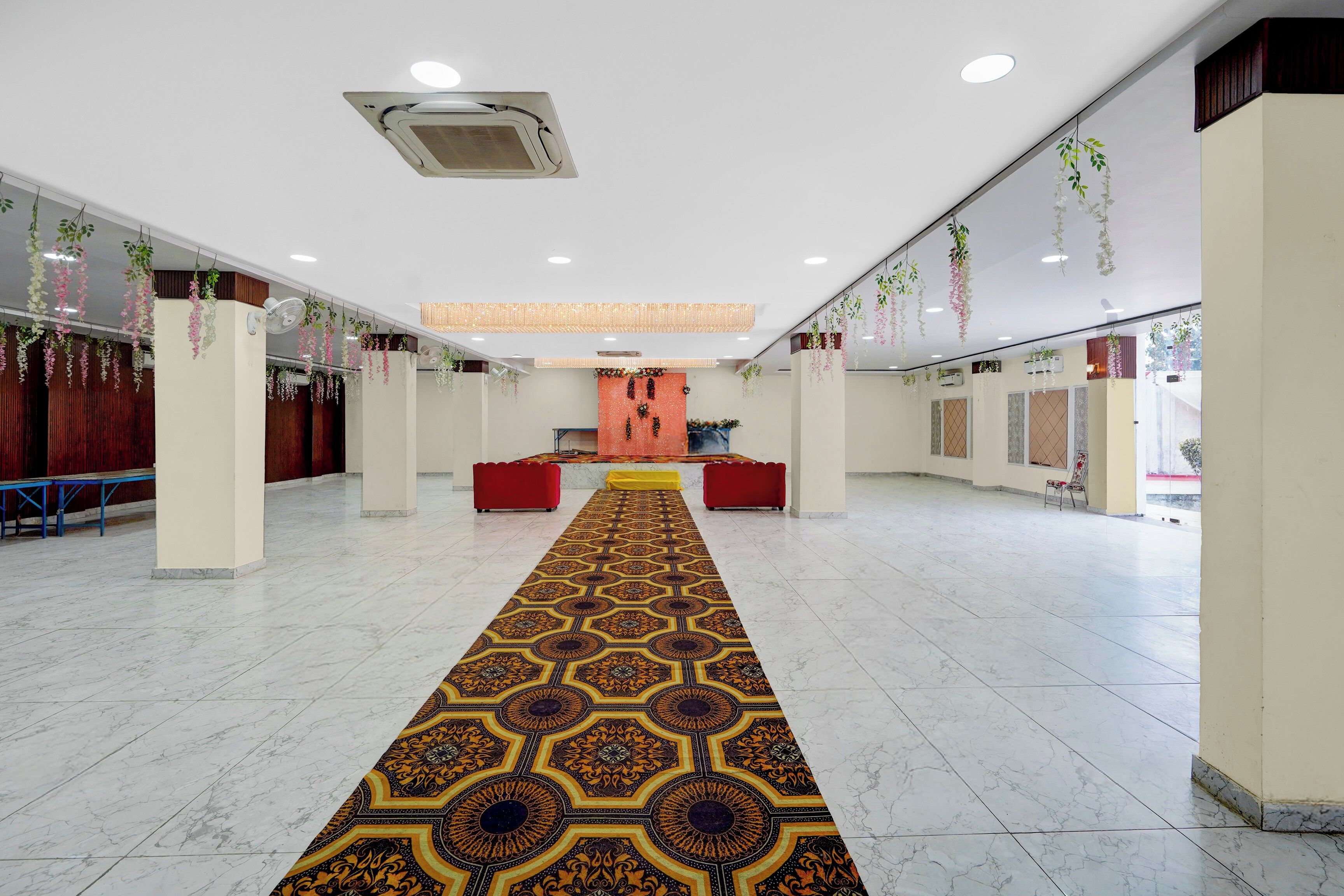 A spacious hall with a patterned carpet, seating areas, and hanging plants.