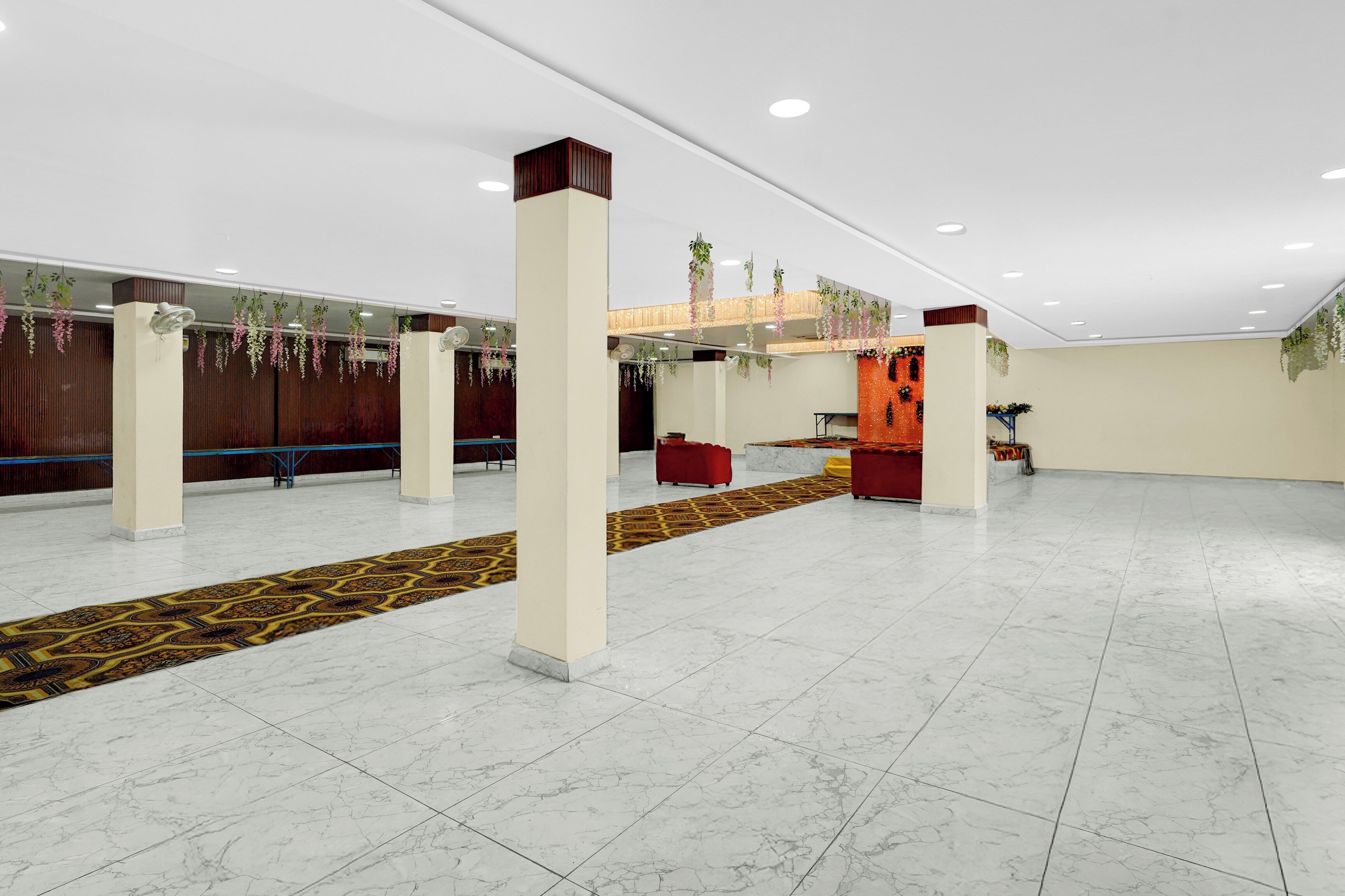 A spacious hall with white marble flooring, a patterned carpet, and hanging plants.